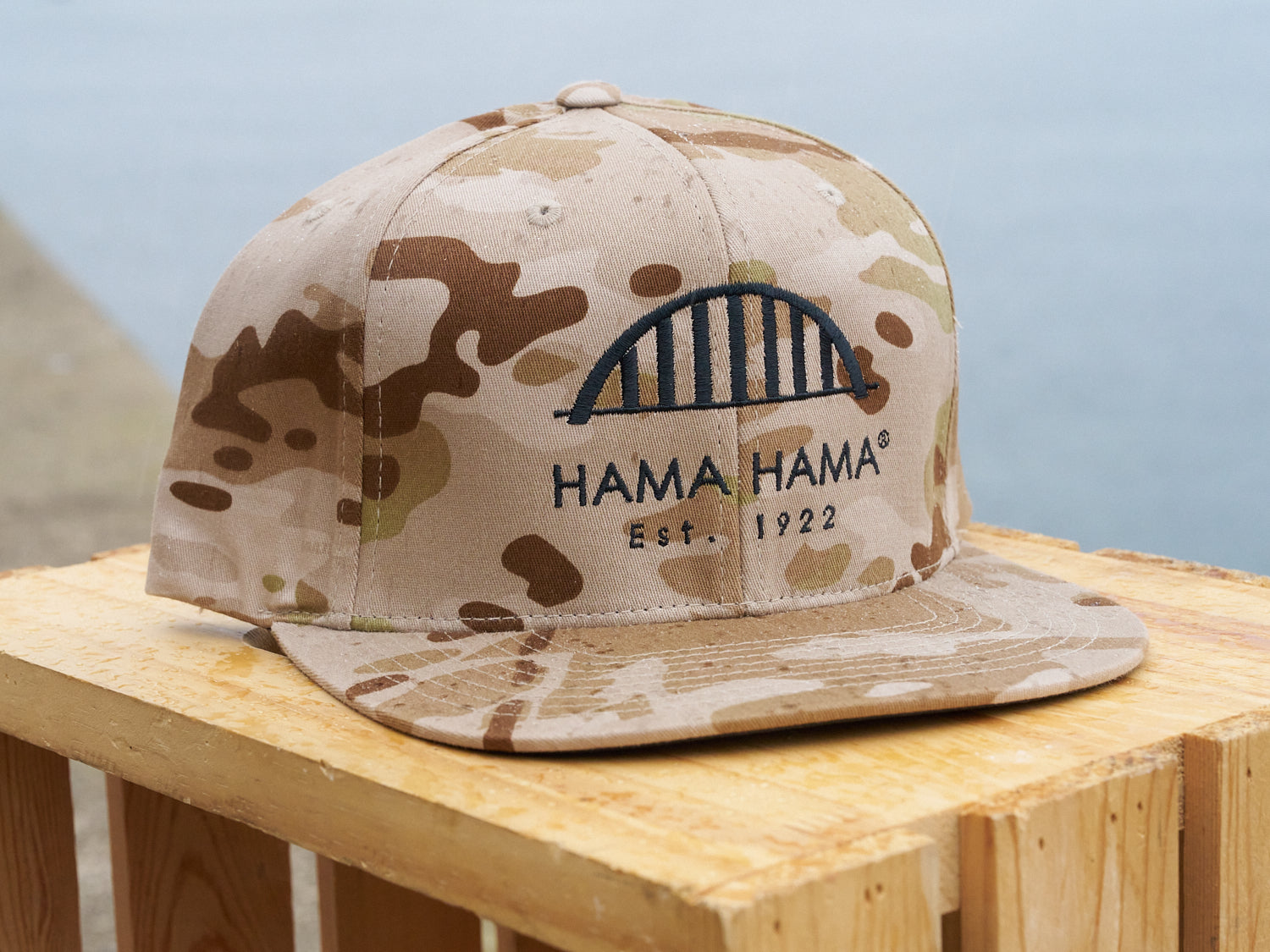 Camouflage-patterned cap with 'HAMA HAMA' branding on a wooden surface.