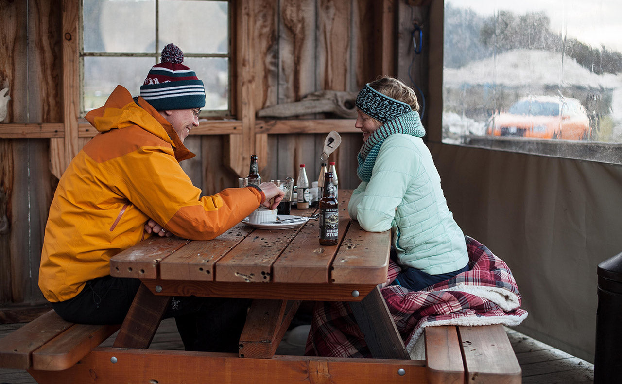 two people sit at an a frame table, smiling with food